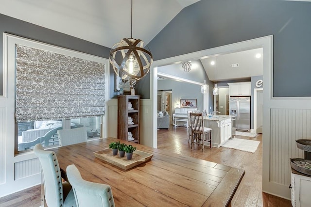 dining room featuring a notable chandelier, light hardwood / wood-style flooring, sink, and high vaulted ceiling