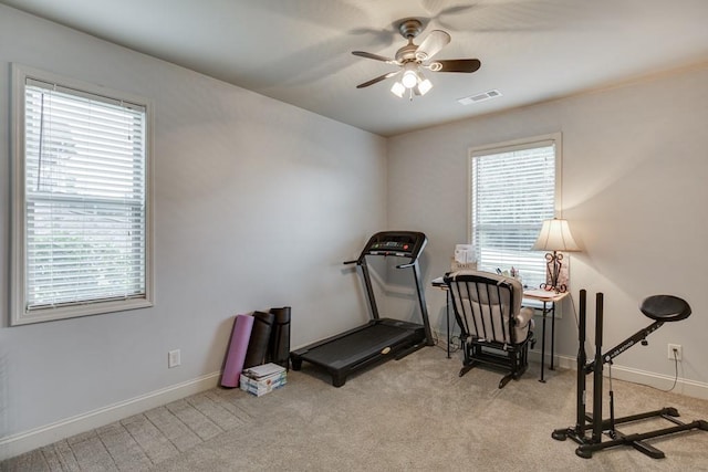 exercise room featuring light colored carpet, ceiling fan, and a wealth of natural light