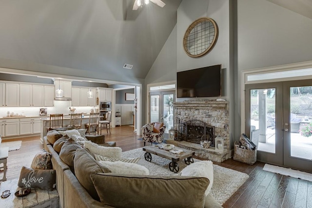 living room featuring hardwood / wood-style floors, ceiling fan, a fireplace, high vaulted ceiling, and french doors