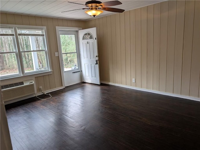 empty room with ceiling fan, a wall mounted AC, dark wood finished floors, and baseboards