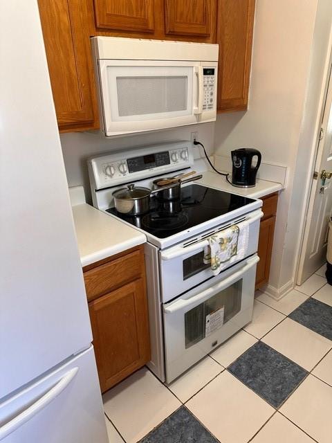 kitchen with brown cabinetry, white appliances, light countertops, and light tile patterned floors