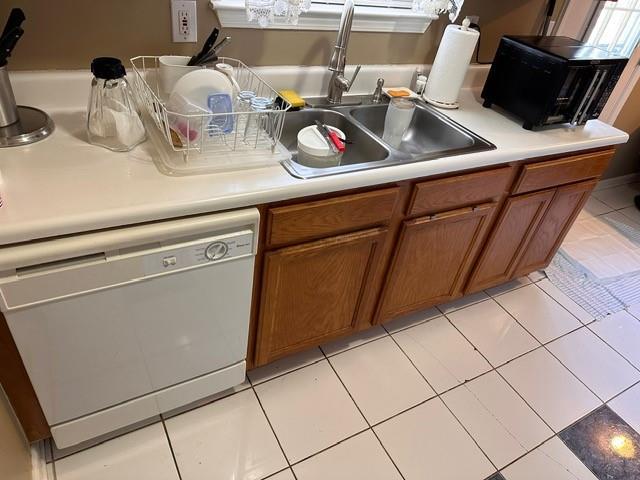 kitchen with light tile patterned floors, dishwasher, brown cabinets, light countertops, and a sink