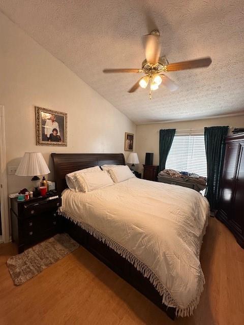 bedroom featuring a ceiling fan, vaulted ceiling, a textured ceiling, and wood finished floors