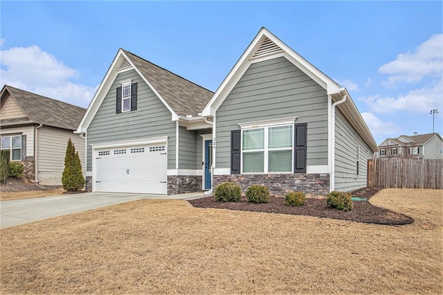 view of front of home with driveway, stone siding, an attached garage, and fence