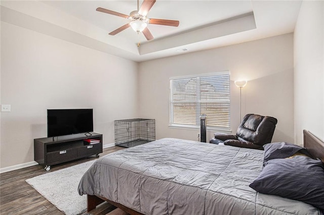 bedroom featuring baseboards, visible vents, a tray ceiling, and wood finished floors