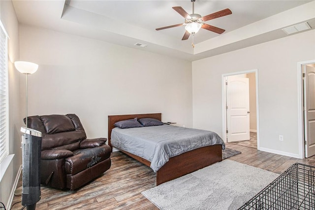 bedroom featuring wood finished floors, a raised ceiling, visible vents, and baseboards