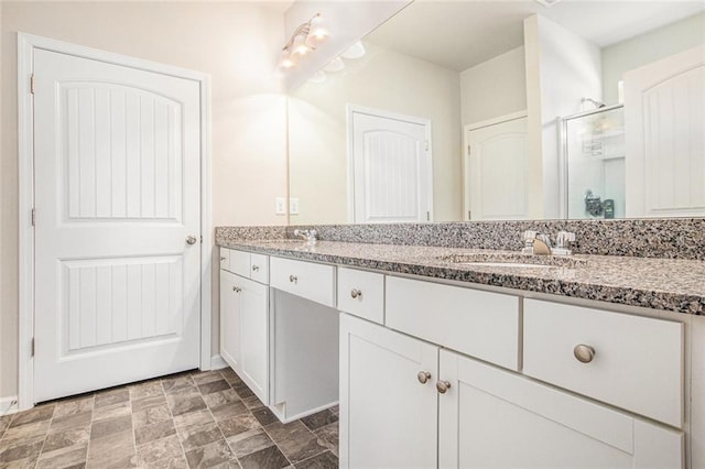 full bath featuring double vanity, a stall shower, stone finish flooring, a sink, and baseboards