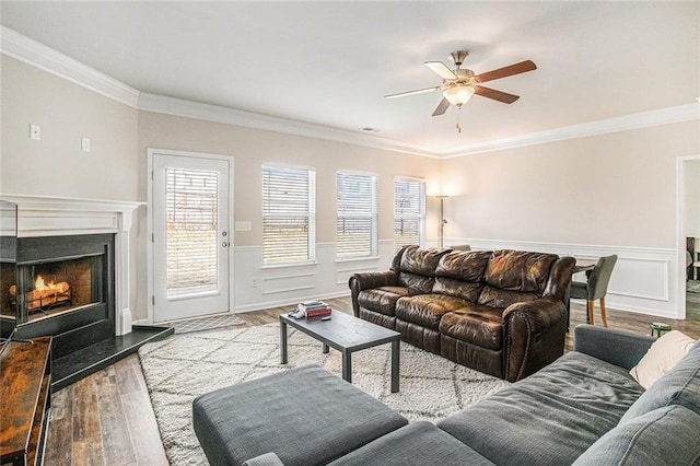 living room with a wainscoted wall, a lit fireplace, ornamental molding, and wood finished floors