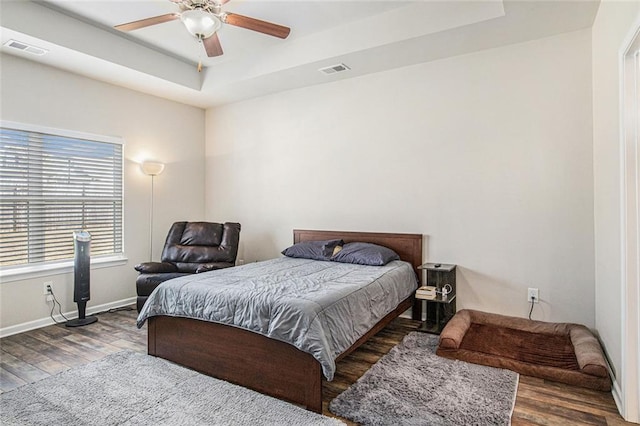 bedroom featuring a tray ceiling, visible vents, baseboards, and wood finished floors