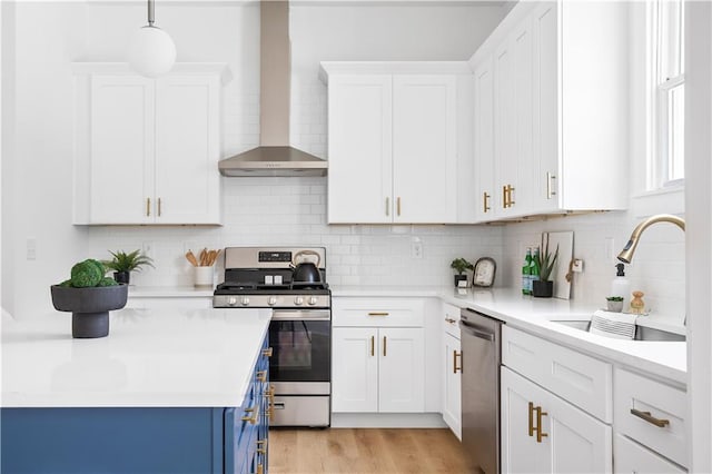 kitchen featuring wall chimney range hood, sink, white cabinets, and appliances with stainless steel finishes