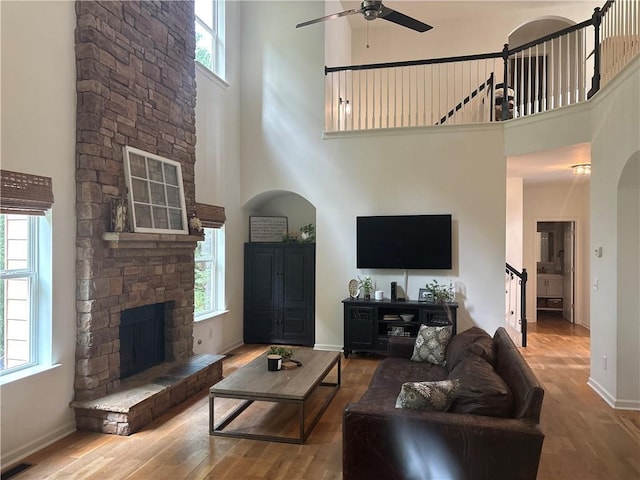 6725 Grove Meadows Ln, Cumming, GA 30028 - living room featuring a towering ceiling, stairs, ceiling fan, wood finished floors, and a stone fireplace