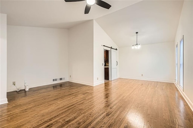 spare room with visible vents, a ceiling fan, wood finished floors, a barn door, and vaulted ceiling