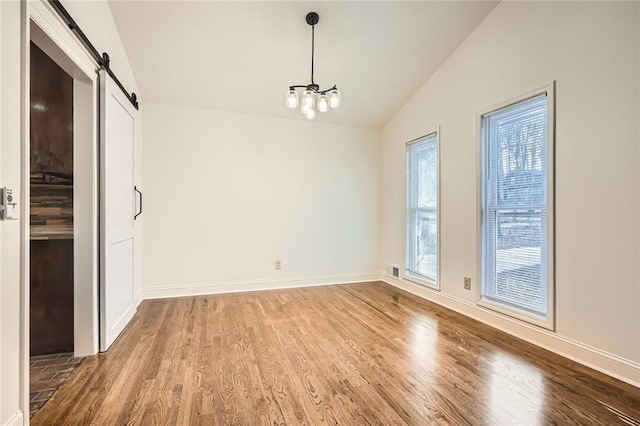 unfurnished dining area featuring a barn door, baseboards, wood finished floors, and vaulted ceiling