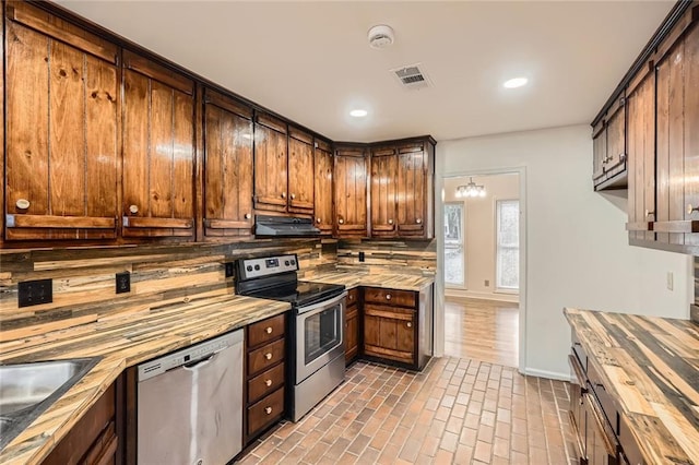 kitchen with visible vents, decorative backsplash, brick floor, exhaust hood, and stainless steel appliances