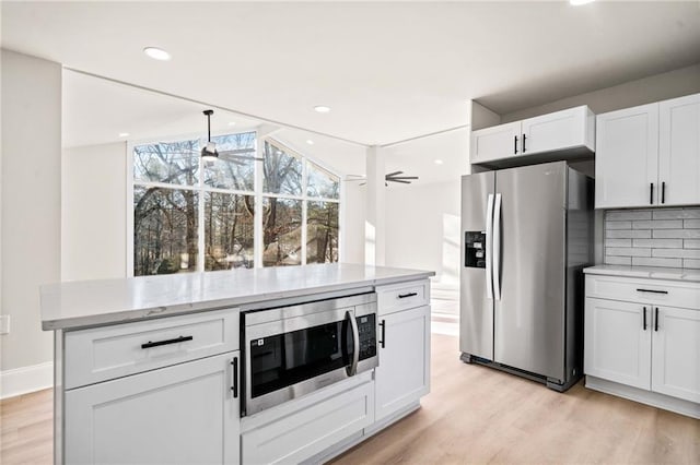 kitchen featuring light hardwood / wood-style flooring, ceiling fan, appliances with stainless steel finishes, tasteful backsplash, and white cabinets