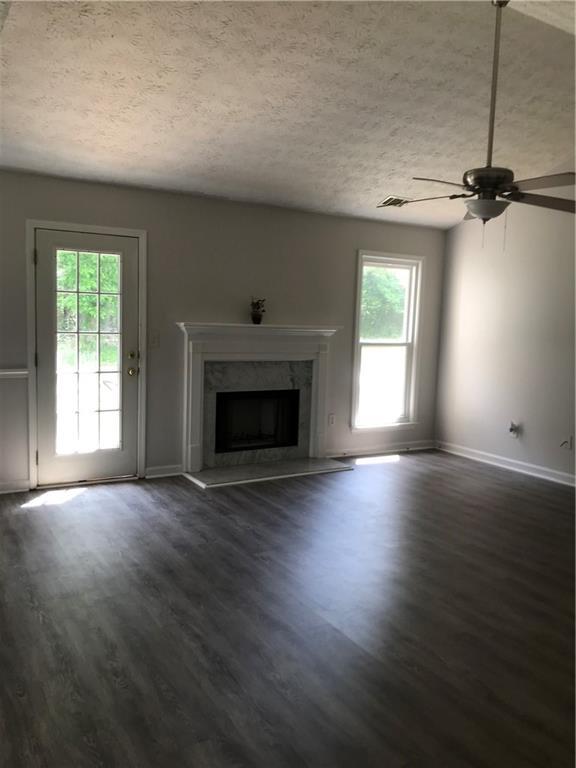 75 Oak Hill Dr, Covington, GA 30016 - unfurnished living room with plenty of natural light, a fireplace, a textured ceiling, ceiling fan, and dark wood-style flooring