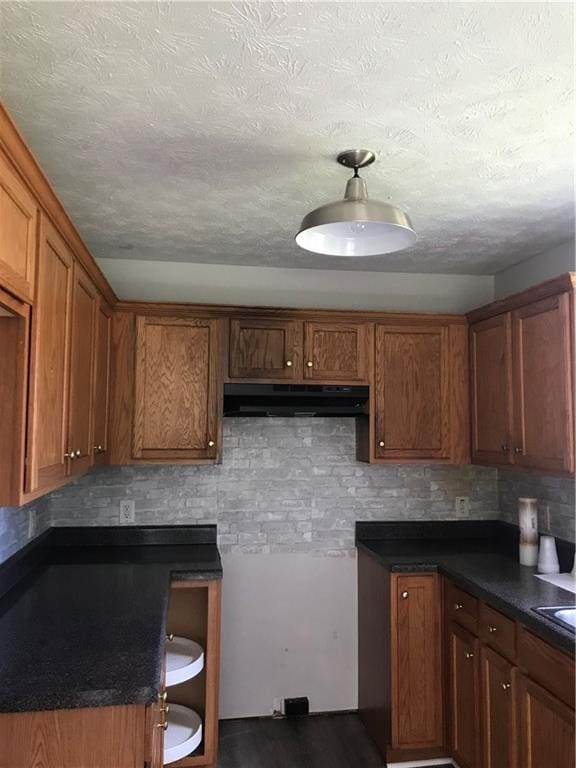 75 Oak Hill Dr, Covington, GA 30016 - kitchen featuring exhaust hood, brown cabinets, decorative backsplash, dark countertops, and a textured ceiling