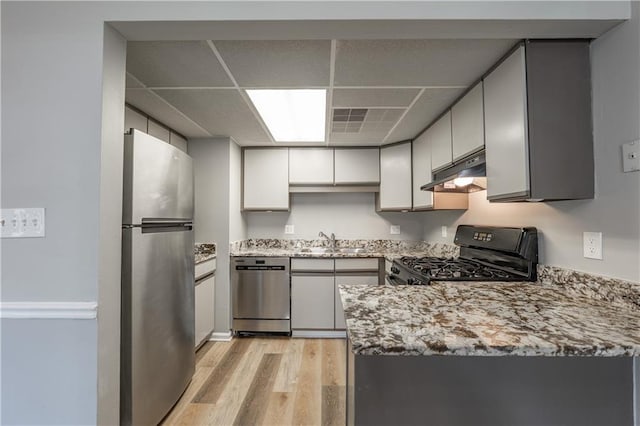 kitchen featuring appliances with stainless steel finishes, under cabinet range hood, a sink, a drop ceiling, and light wood-type flooring