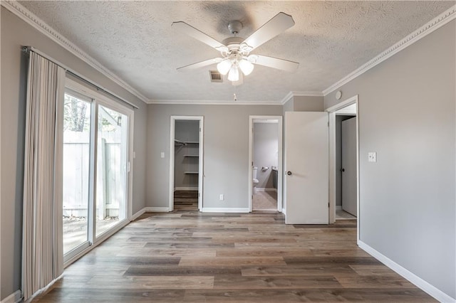 unfurnished bedroom with wood finished floors, access to exterior, a textured ceiling, a spacious closet, and ornamental molding