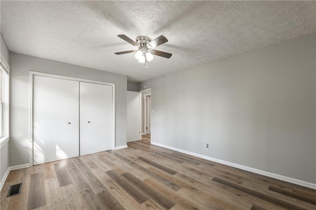 unfurnished bedroom featuring baseboards, wood finished floors, a closet, a textured ceiling, and a ceiling fan