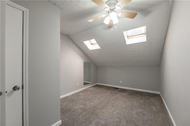 additional living space with a skylight, vaulted ceiling, a textured ceiling, carpet floors, and baseboards