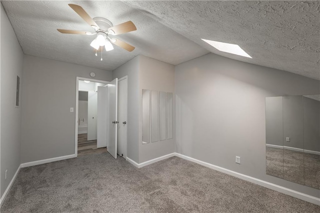 unfurnished bedroom featuring carpet floors, a skylight, baseboards, vaulted ceiling, and a textured ceiling