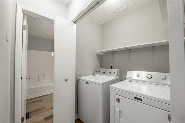 laundry room with a textured ceiling, separate washer and dryer, and light wood-type flooring