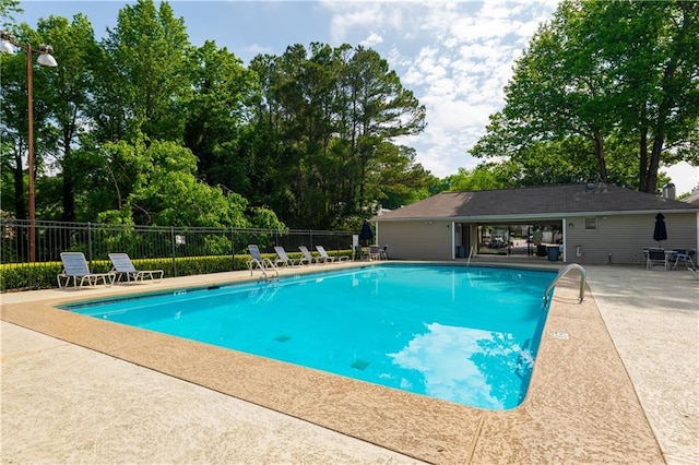 community pool with fence, a patio area, and view of scattered trees