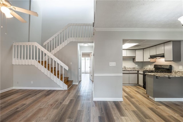 kitchen with under cabinet range hood, stainless steel gas range oven, wood finished floors, a ceiling fan, and gray cabinetry