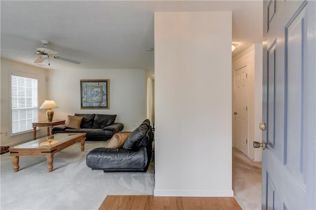 living room with baseboards, a ceiling fan, light wood-style flooring, and light colored carpet