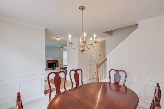 dining room with a decorative wall, a ceiling fan, a chandelier, stairs, and wainscoting