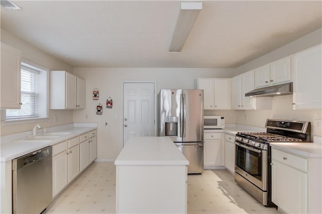 kitchen with appliances with stainless steel finishes, light floors, under cabinet range hood, a sink, and a kitchen island