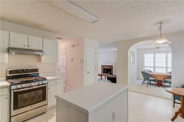 kitchen featuring stainless steel range with gas stovetop, under cabinet range hood, arched walkways, a brick fireplace, and light countertops