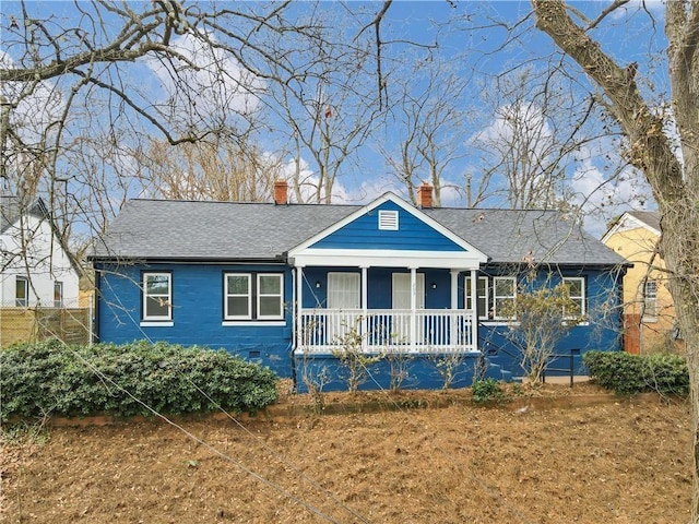 view of front of house featuring a chimney, a porch, and roof with shingles