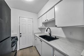 kitchen with a sink, white cabinets, range, freestanding refrigerator, and light wood finished floors