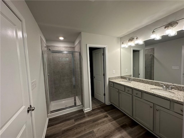 full bathroom with wood finished floors, baseboards, double vanity, a stall shower, and a sink