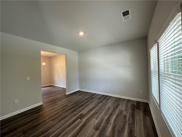 unfurnished room featuring visible vents, baseboards, and dark wood finished floors