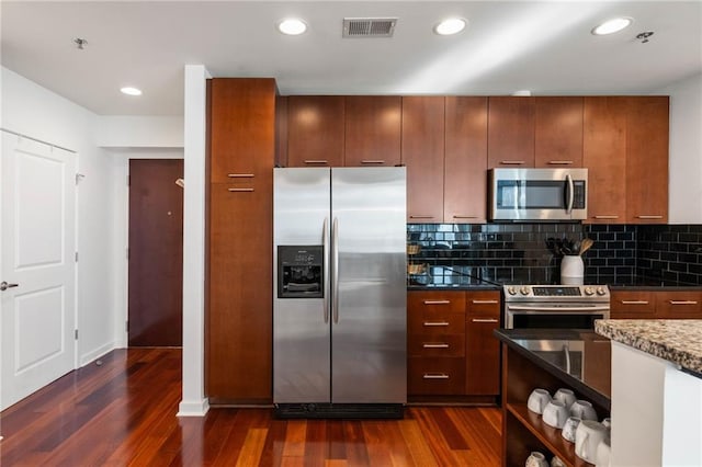 kitchen with stainless steel appliances, decorative backsplash, dark hardwood / wood-style flooring, and dark stone counters