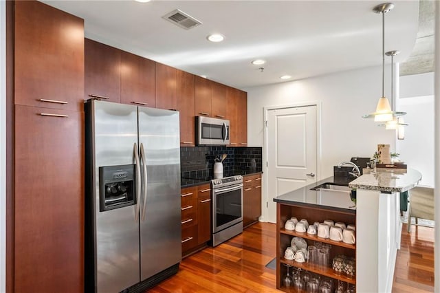 kitchen with appliances with stainless steel finishes, dark wood-type flooring, tasteful backsplash, sink, and kitchen peninsula