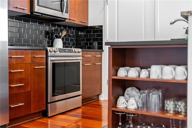 kitchen with tasteful backsplash, white cabinets, appliances with stainless steel finishes, and light hardwood / wood-style flooring