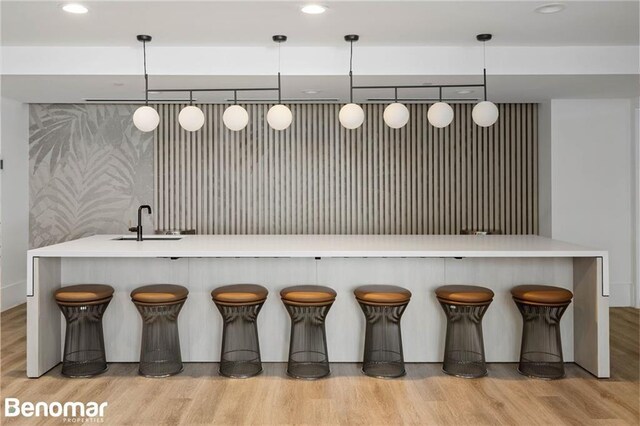 bar with light hardwood / wood-style floors, sink, and hanging light fixtures