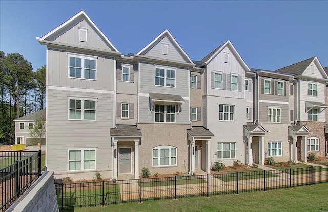 townhome / multi-family property with brick siding, board and batten siding, and a fenced front yard