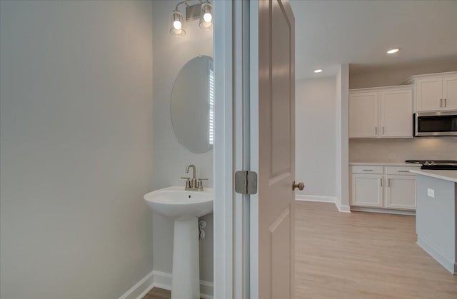 bathroom with recessed lighting, decorative backsplash, a sink, wood finished floors, and baseboards