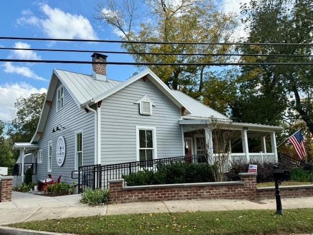 view of front of property featuring covered porch, metal roof, and a chimney