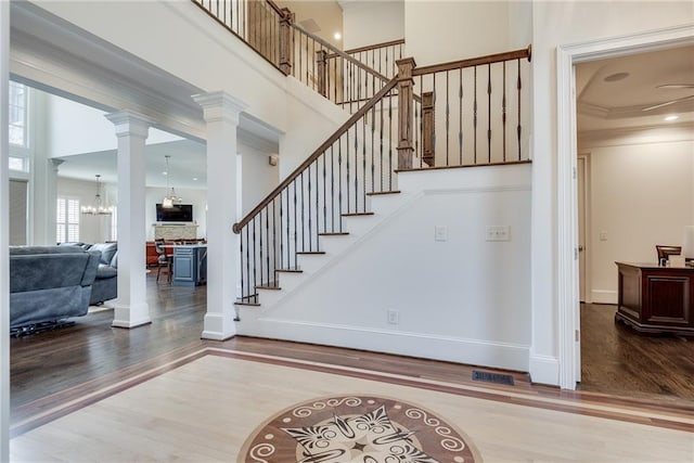 stairs featuring wood-type flooring, ornamental molding, ornate columns, a towering ceiling, and a notable chandelier