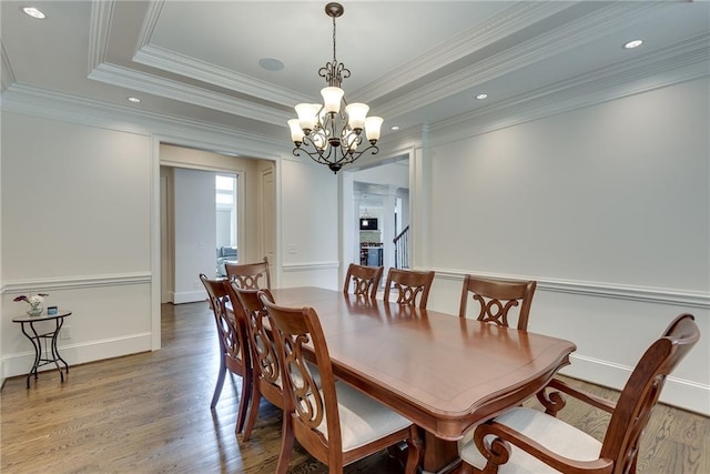 dining space with a raised ceiling, wood-type flooring, ornamental molding, and a chandelier