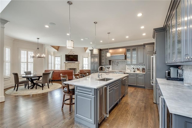 kitchen featuring a large island with sink, sink, pendant lighting, gray cabinets, and light stone counters