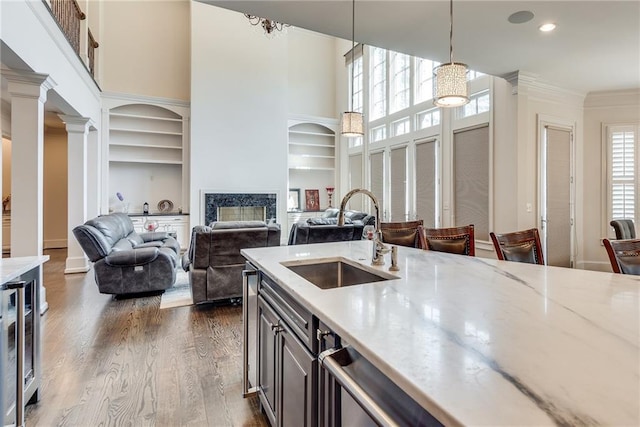 kitchen with light stone countertops, light wood-type flooring, ornamental molding, pendant lighting, and sink