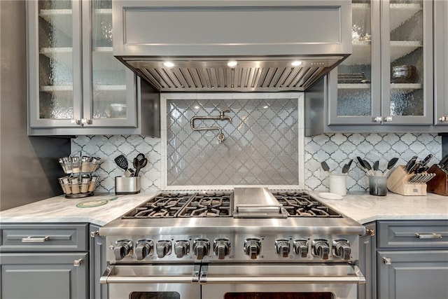 kitchen featuring light stone countertops, wall chimney exhaust hood, decorative backsplash, and stainless steel stove