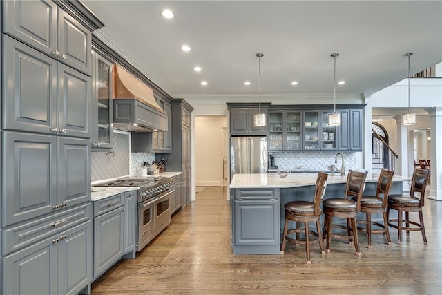 kitchen with hanging light fixtures, an island with sink, appliances with stainless steel finishes, backsplash, and gray cabinetry